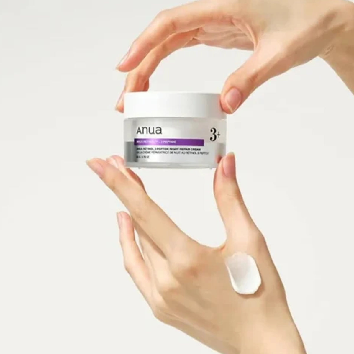 A person's hands holding a white jar of Anua 3+ Advanced Cellular Cream against a clean white background, with a dollop of the white cream shown on the hand.