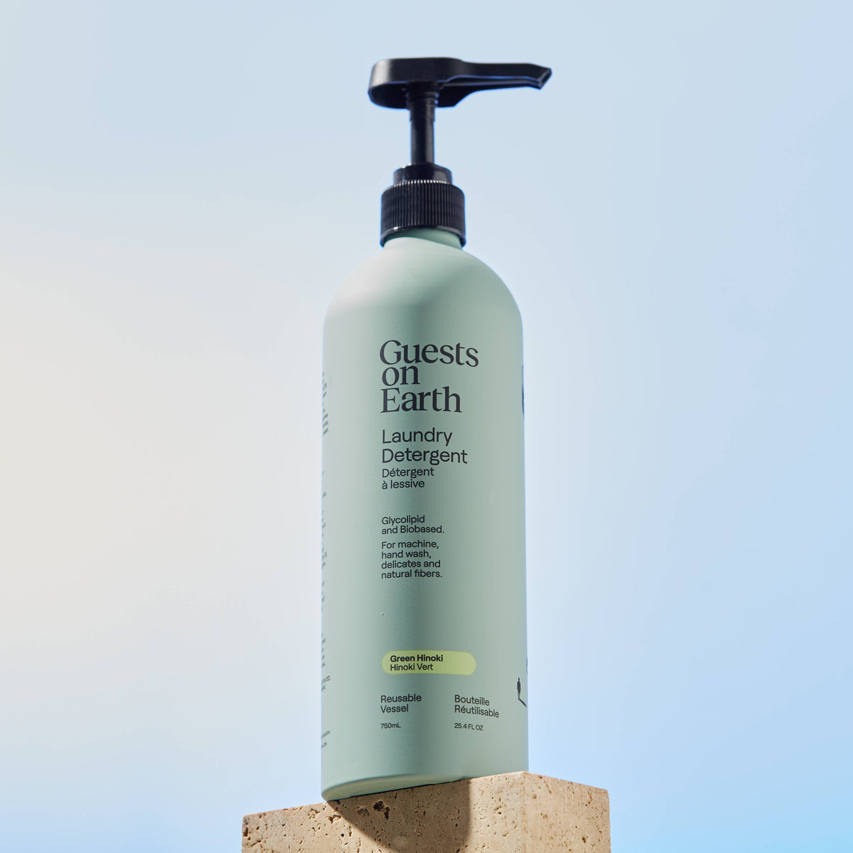 Guests on Earth Green Hinoki Laundry Detergent pump bottle on a block against a blue background.