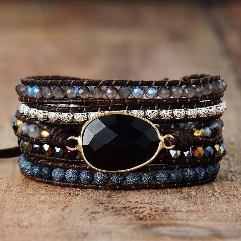 Multistrand bracelet with beads and a large black stone on a wooden surface.