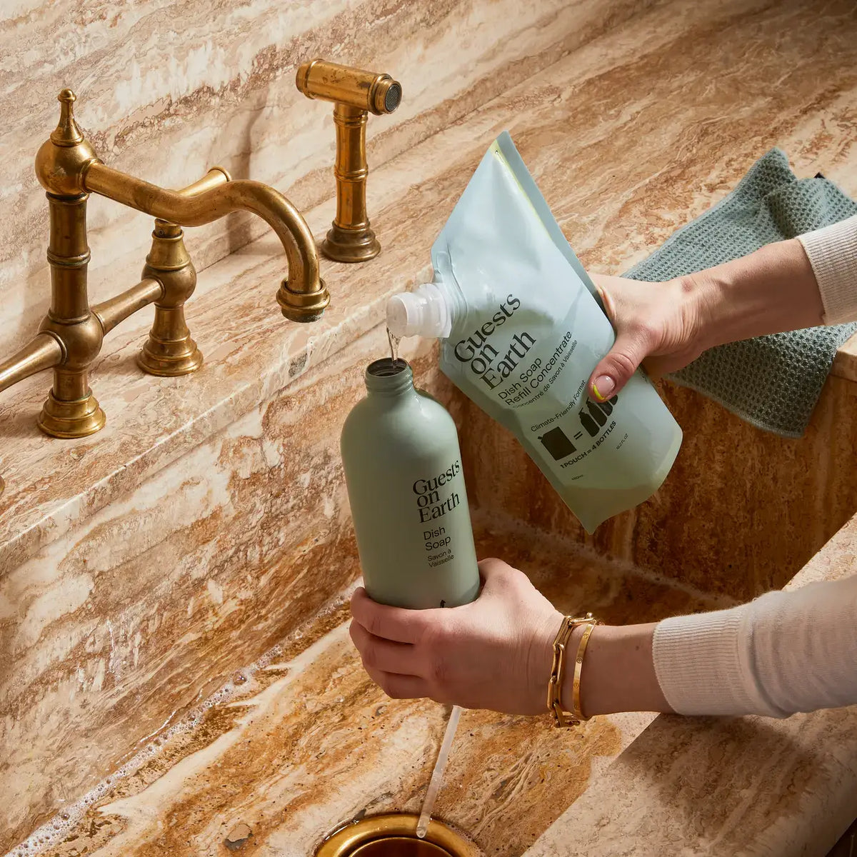 Person refilling a Guests on Earth dish soap bottle from a concentrate pouch at a kitchen sink.
