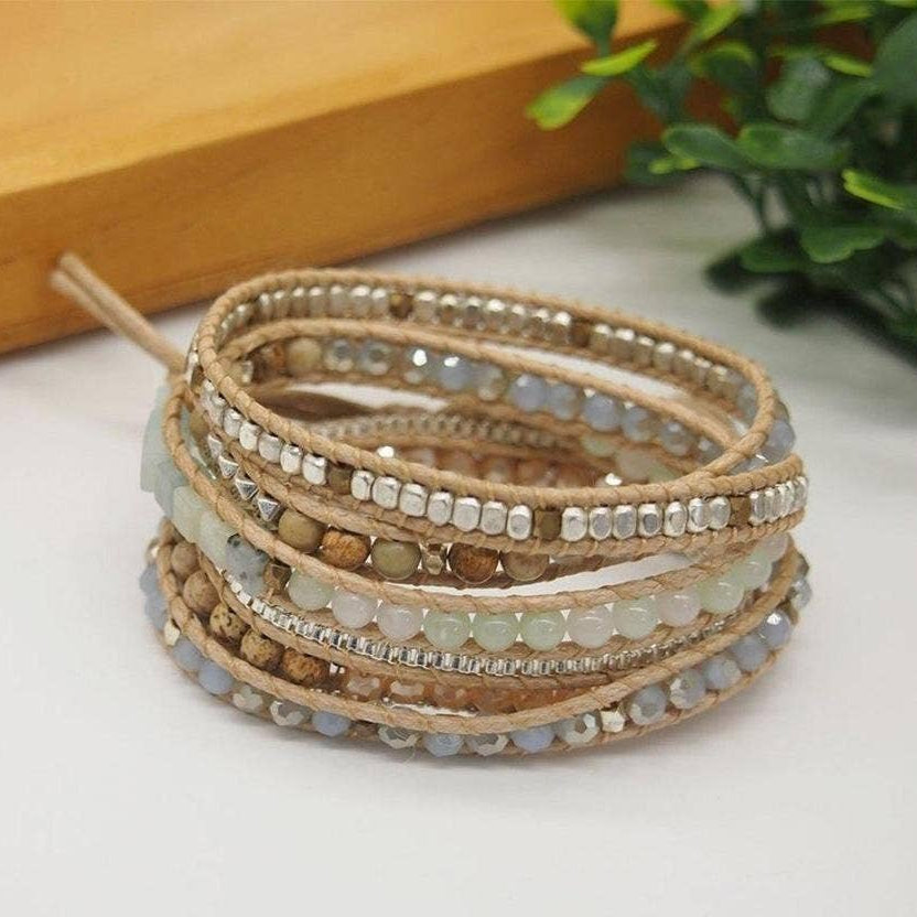 Stack of beaded bracelets on a light surface with a wooden block and plant in the background