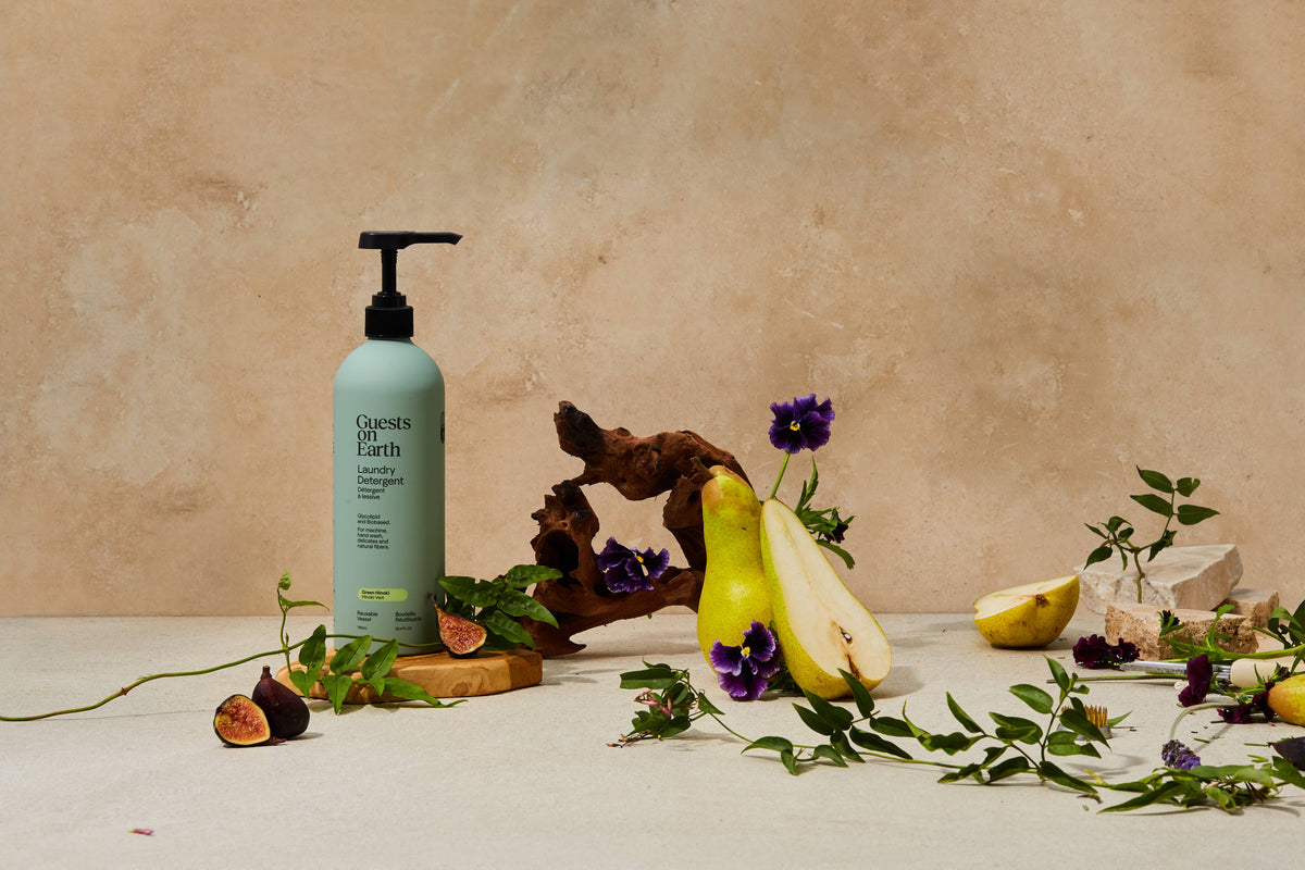 Guests on Earth laundry detergent bottle arranged with cut fruit, flowers and greenery.