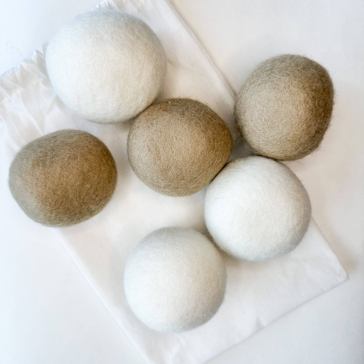 Set of six felted natural wool dryer balls in beige and white on a white surface