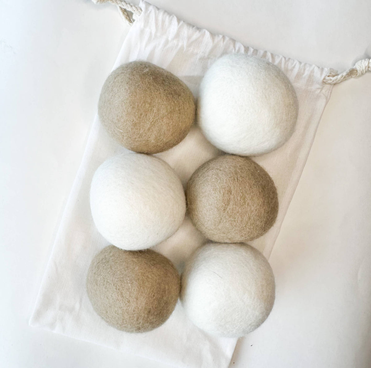 Set of six natural fiber dryer balls in beige and white on a white background