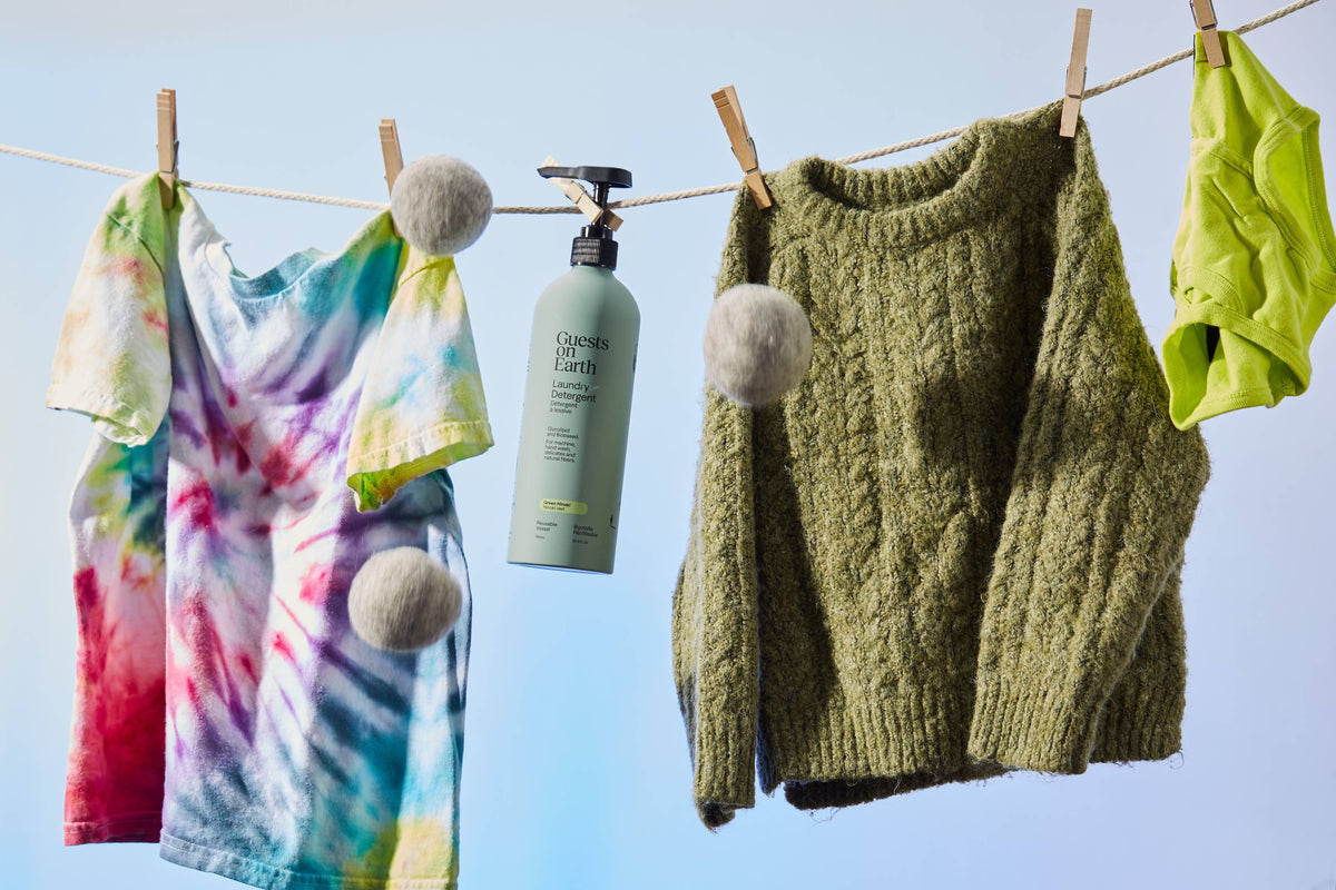 Guests on Earth laundry detergent bottle hanging with a sweater, colourful shirt and wool dryer balls.