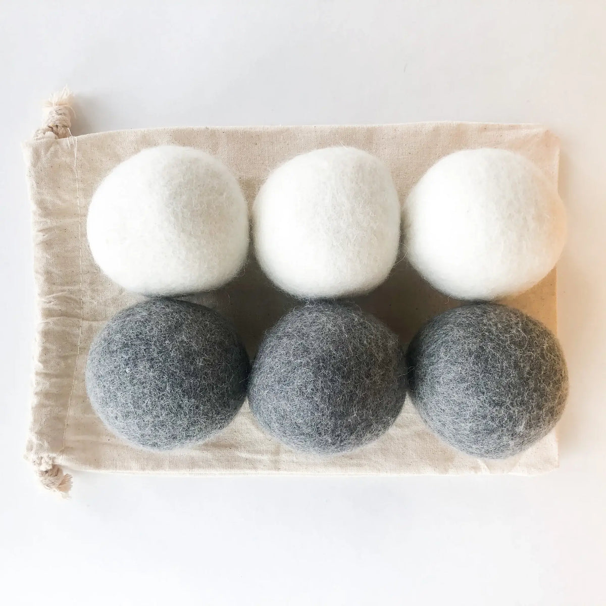 Set of six natural dryer balls, three white and three gray, on a beige fabric background.
