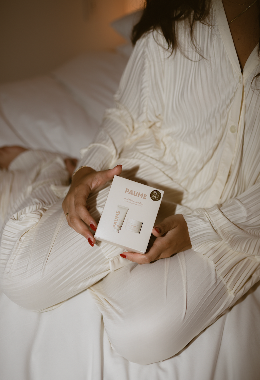 Person holding a skincare product box labeled 'PAUME' in a white robe.