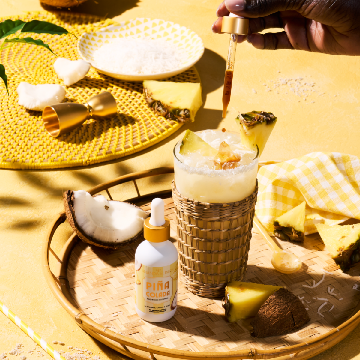 Pina Colada elixir being poured into a glass with a bottle of Pina Colada on a yellow table.