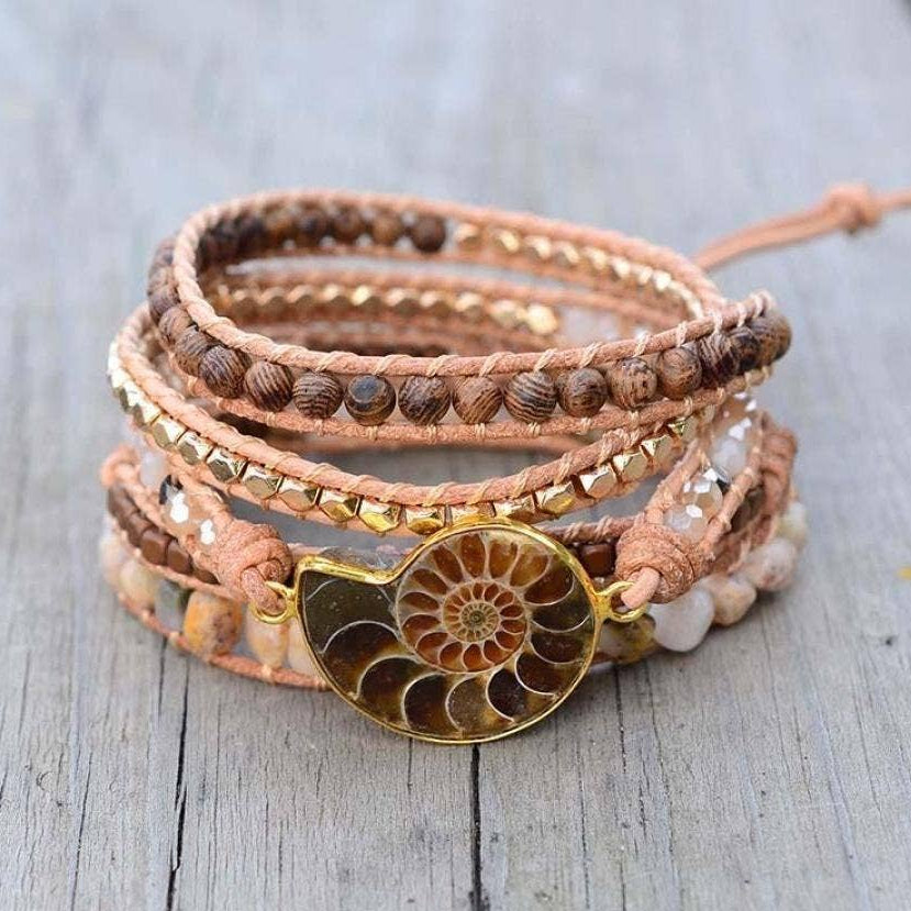 Multi-layered bracelet with a gold ammonite fossil charm on a wooden surface.