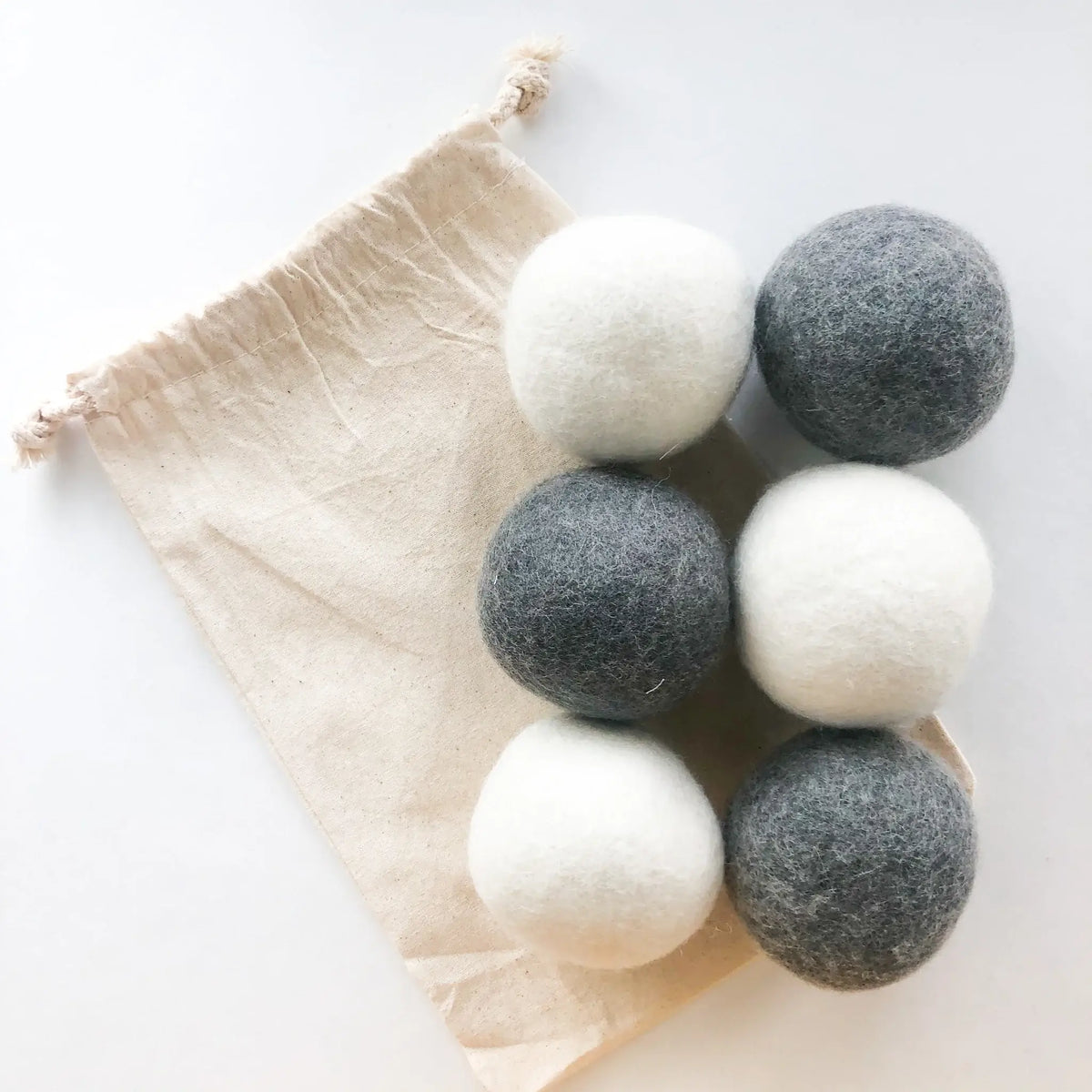 Set of six felted wool dryer balls in white and gray on a beige drawstring bag against a white background.
