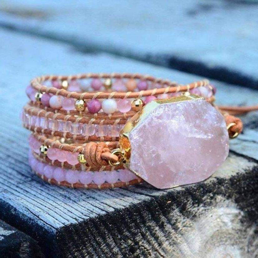 Stack of beaded bracelets with a prominent pink stone on a wooden surface.