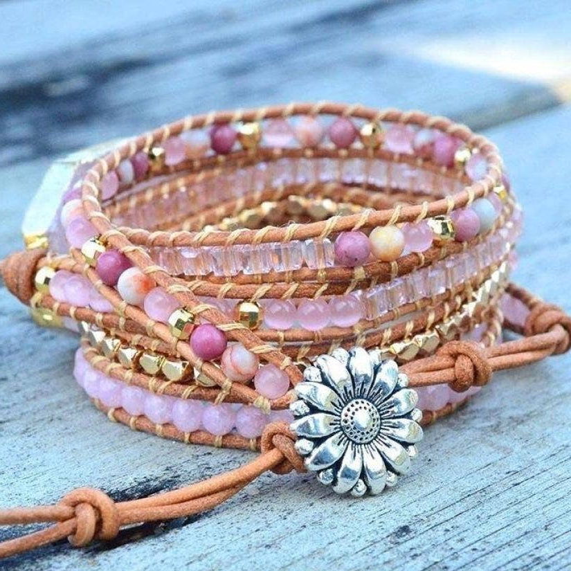 Multi-layered bracelet with pink beads and a sunflower charm on a wooden surface.
