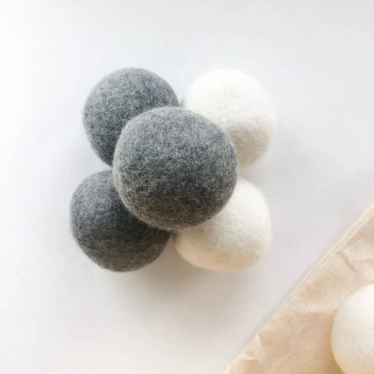 Three all natural dryer balls, two gray and one white, on a light surface.