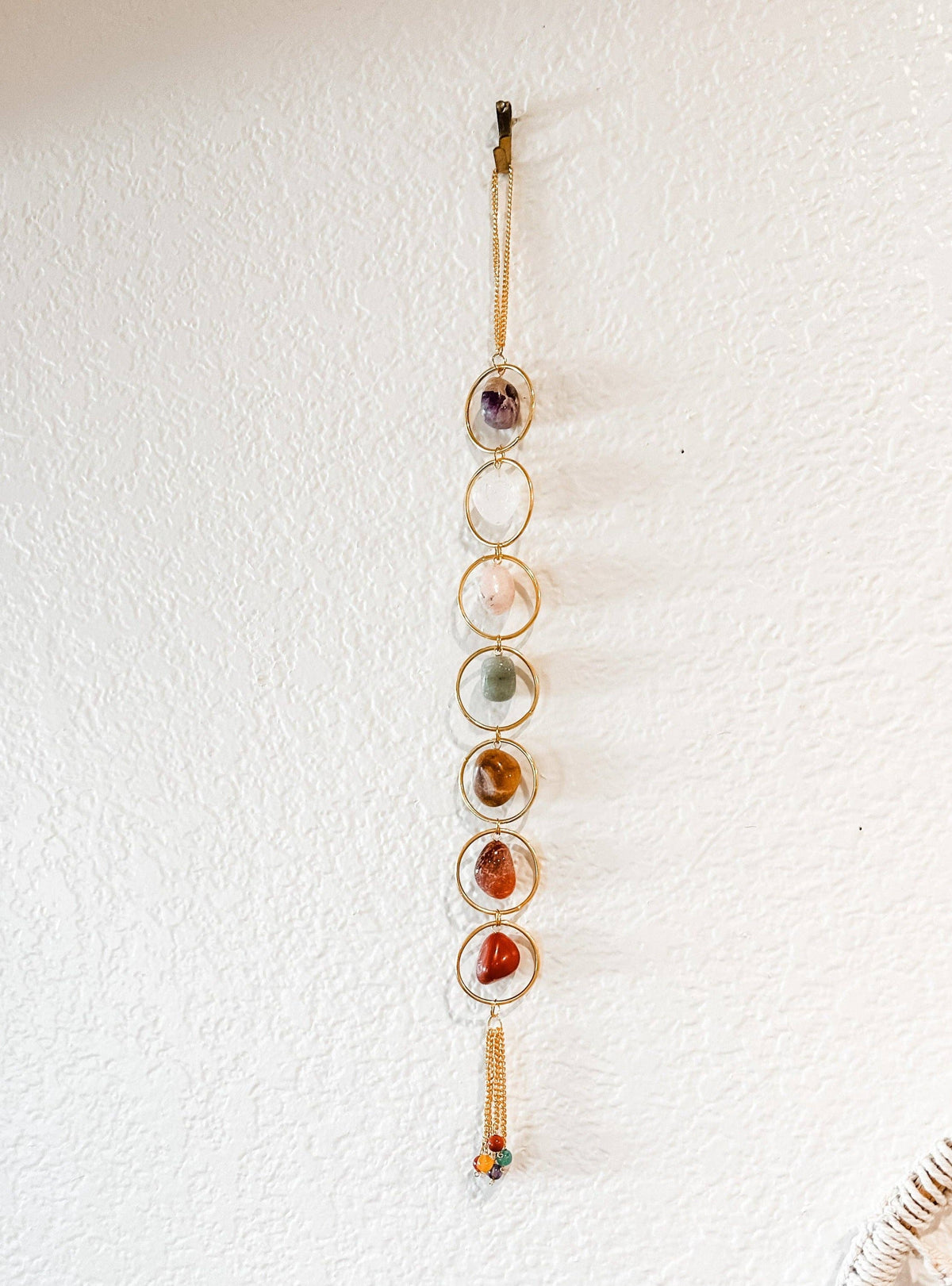 Seven Chakra Crystal Wall Hanging with circular stones on a textured white wall