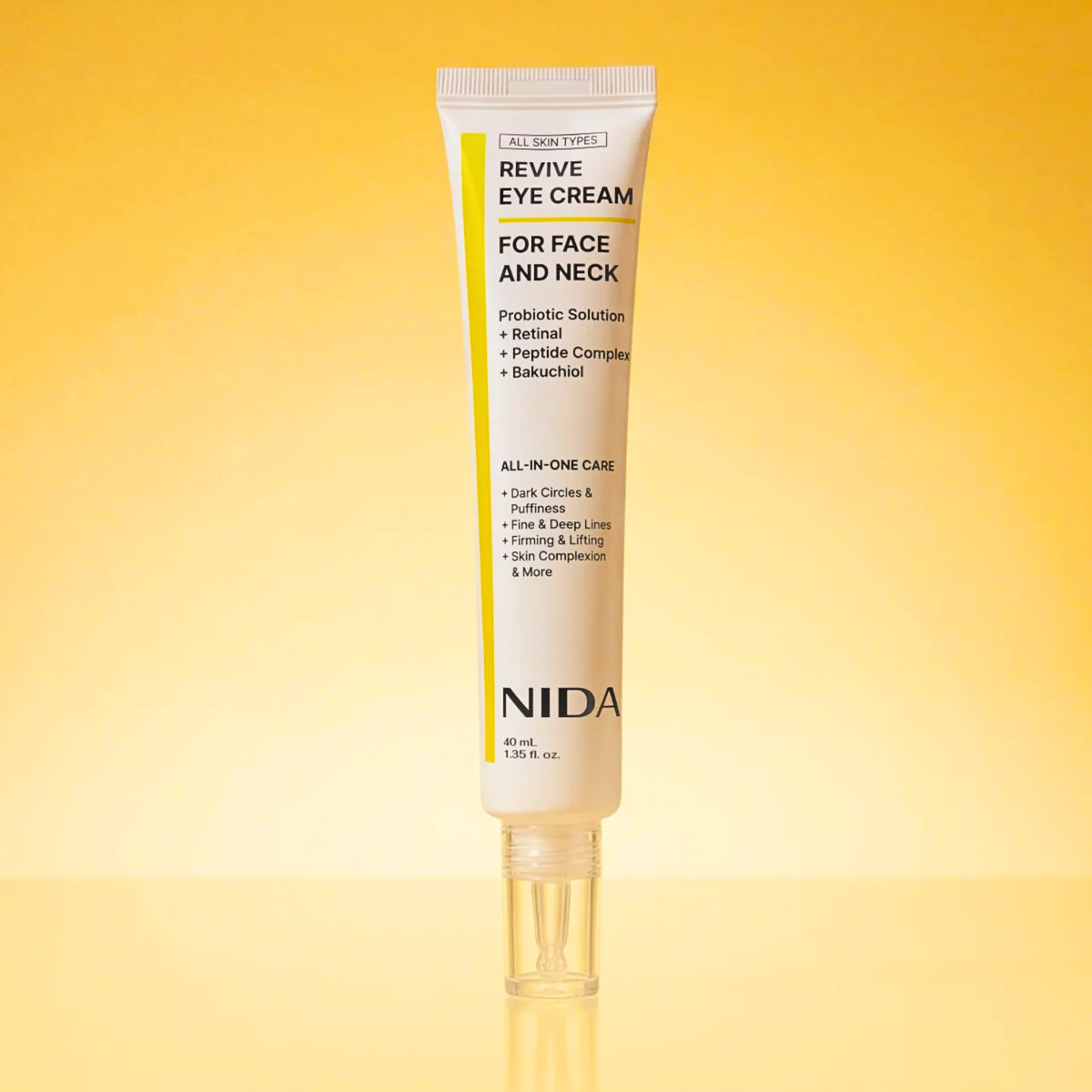 A single tube of NIDA Revive Eye Cream for face and neck, displayed vertically on a reflective surface against a warm yellow-to-gold gradient background.