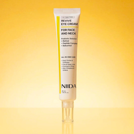 A single tube of NIDA Revive Eye Cream for face and neck, displayed vertically on a reflective surface against a warm yellow-to-gold gradient background.