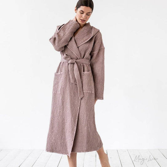 A woman wearing a long, textured waffle-knit bathrobe in a dusty mauve-pink color, standing against a clean white studio background.