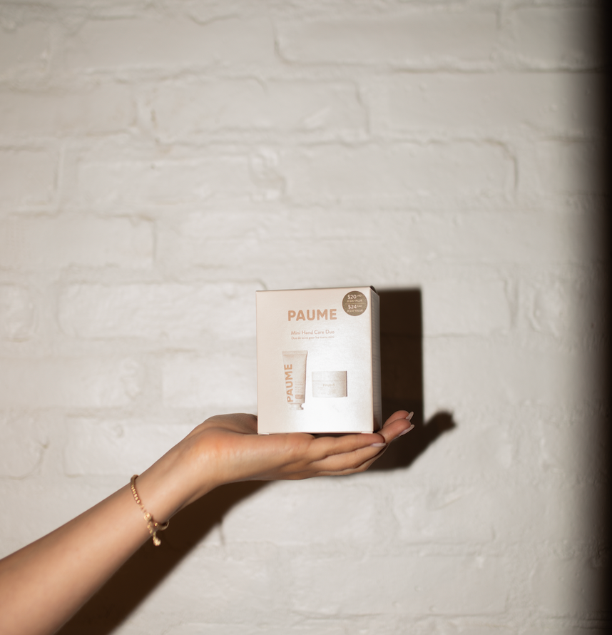 Hand holding a Paume box against a textured white wall