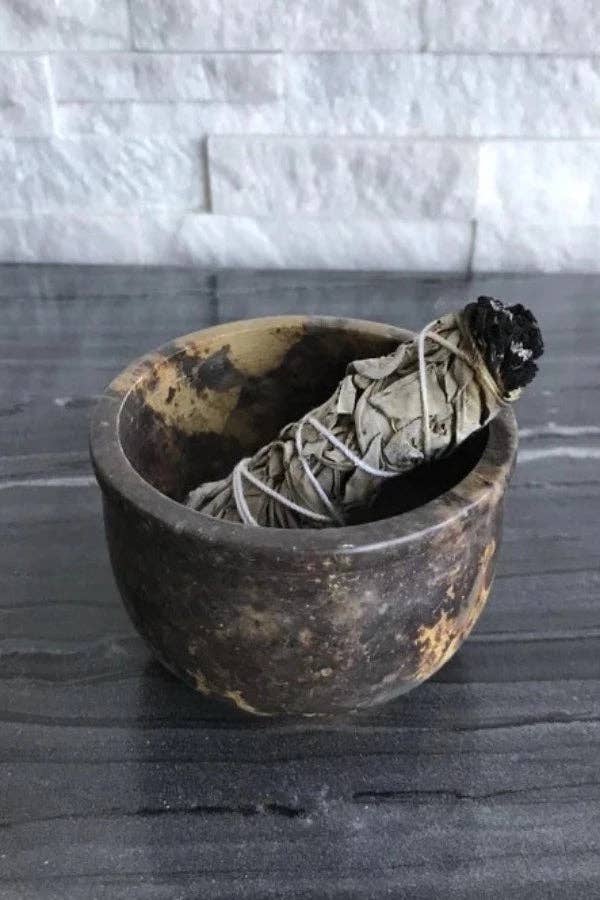 Smoldering sage in a Soapstone Smudging Bowl on a dark surface with a tiled wall background