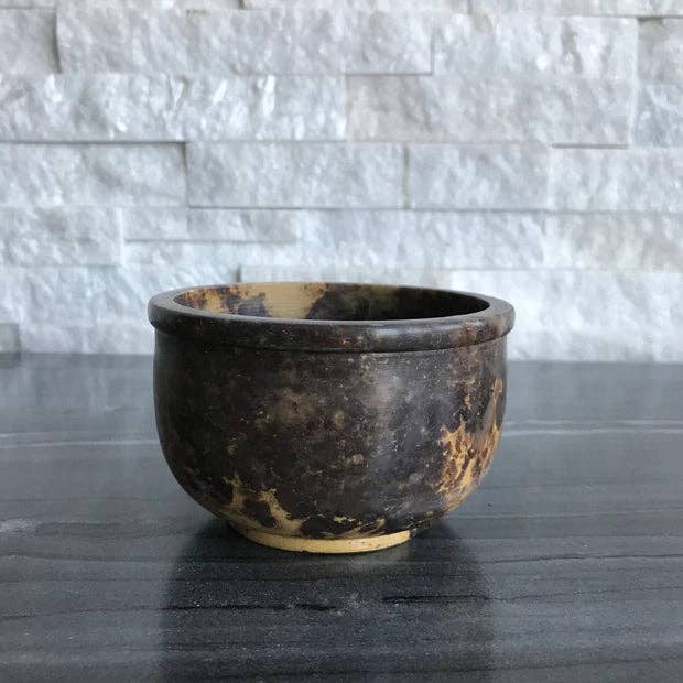 Soapstone Smudging Bowl on a dark surface with a light stone wall background