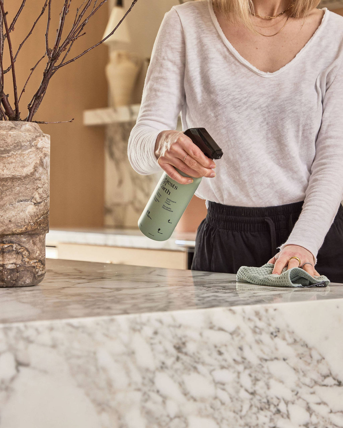 Person using Guests on Earth spray cleaner and a cloth on a stone countertop.