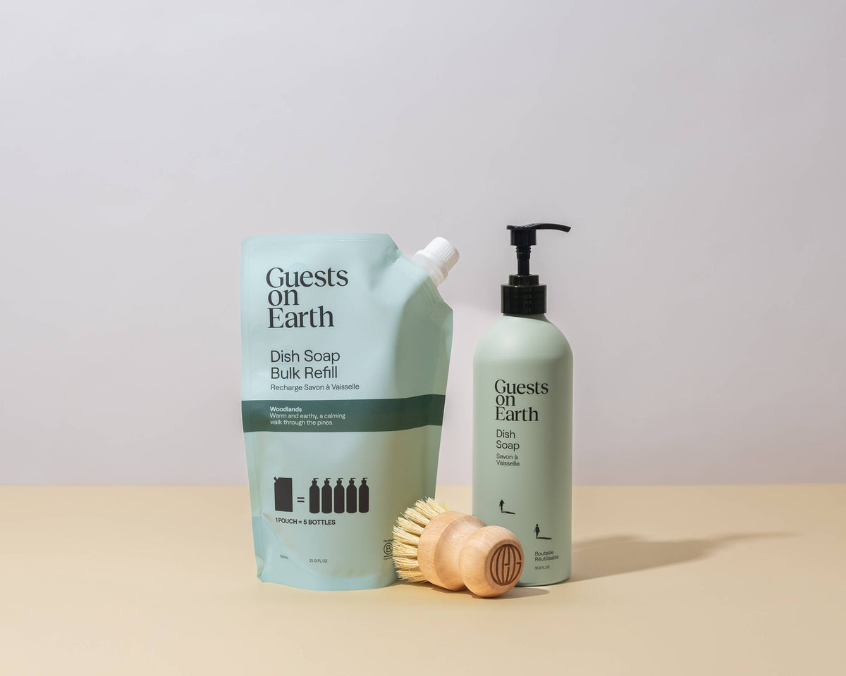 Guests on Earth Woodlands Dish Soap refill pouch and pump bottle beside a wooden dish brush.