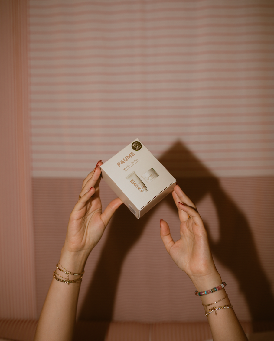 Person holding a small box with 'PAUME' branding against a striped wall.