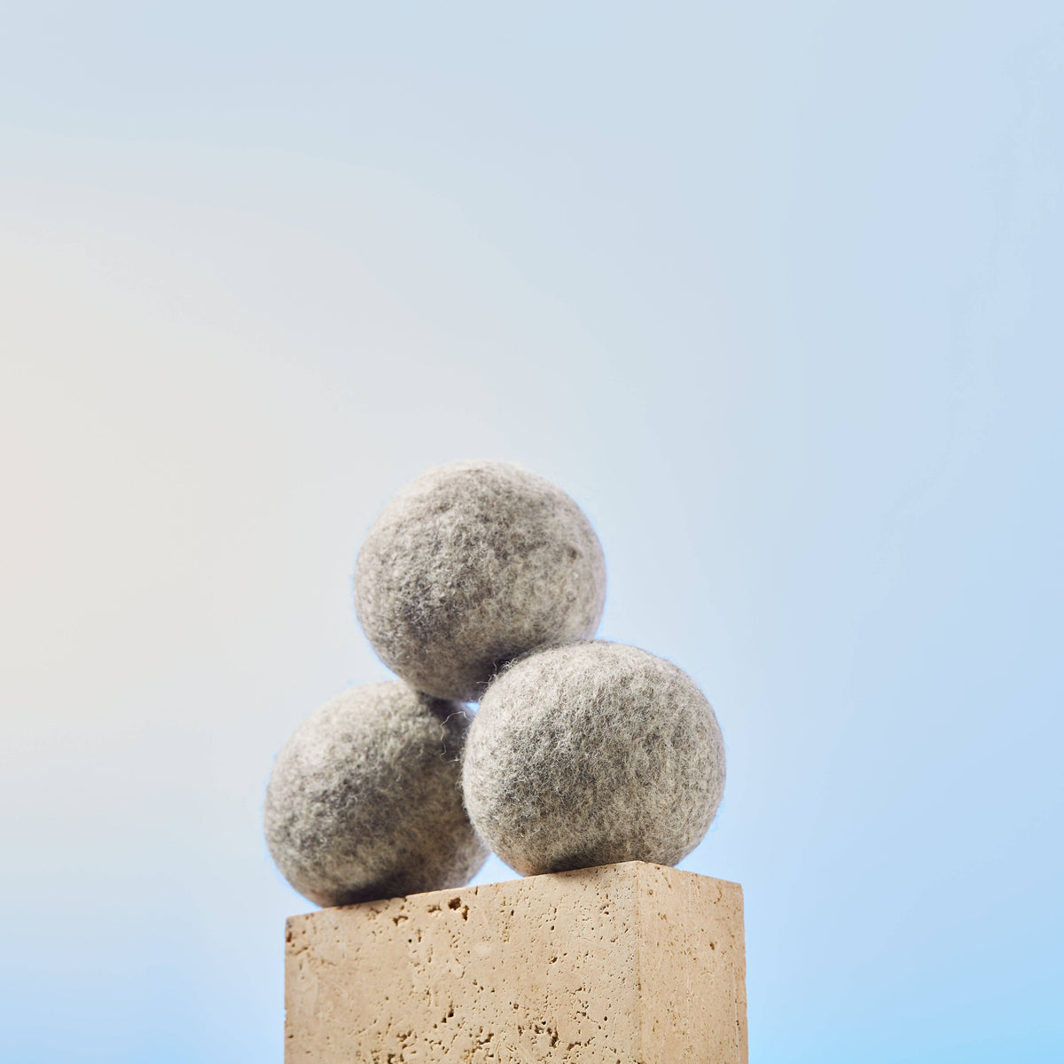 Three wool dryer balls stacked on a block against a blue background.