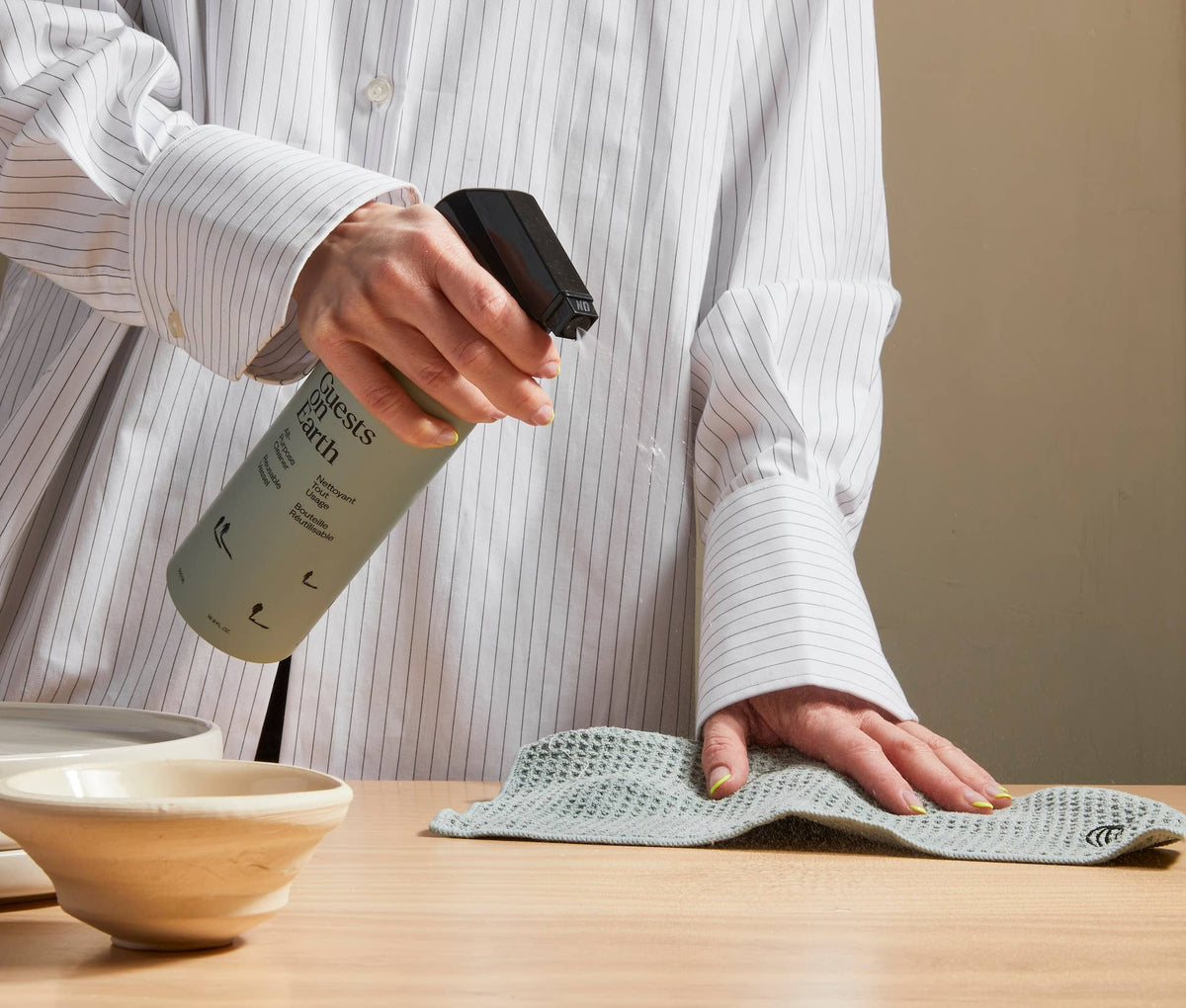 Person spraying Guests on Earth cleaner beside a folded cloth on a wooden table.