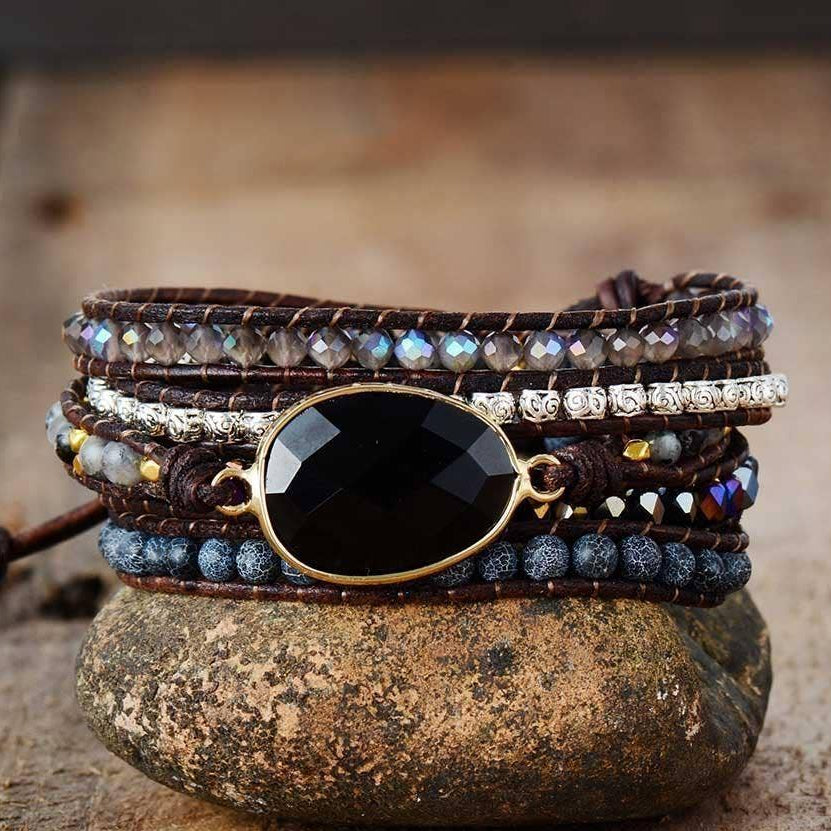 Multistrand beaded bracelet with a large black stone on a stone surface.